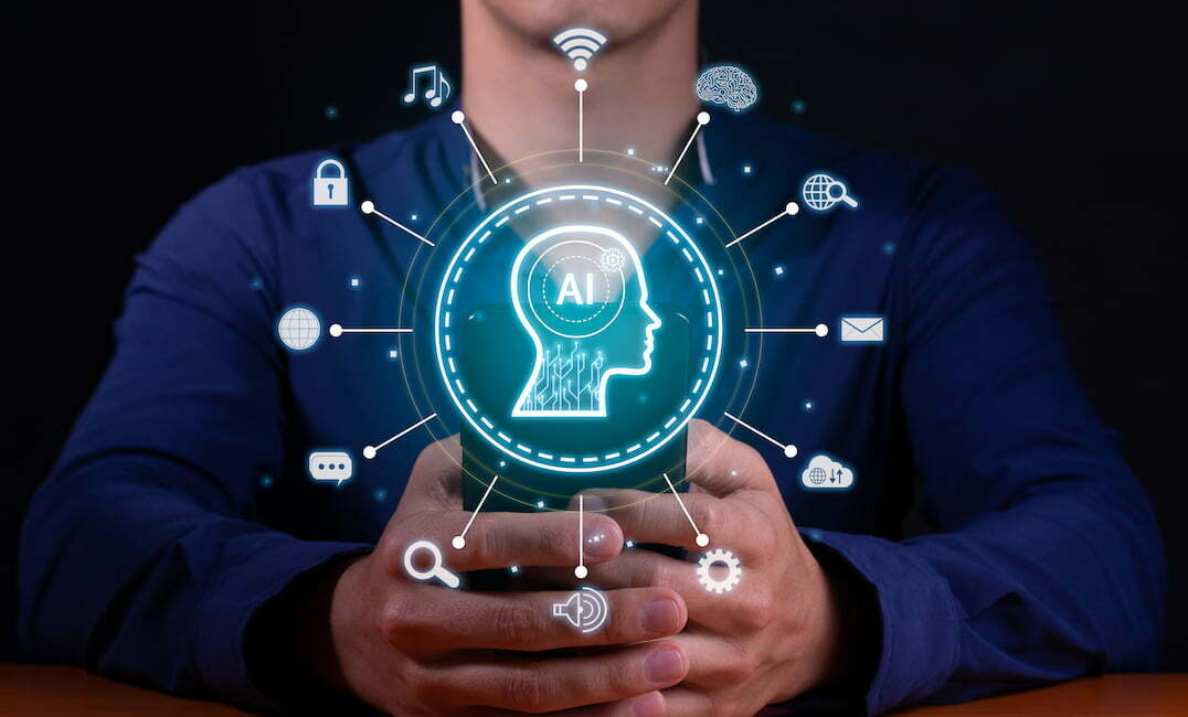 A photo of a man holding his mobile phone typing with an AI hologram overlay of a brain with a circle of icons including a lock, envelope, magnifying glass, cloud, world, sound, and other icons.